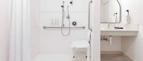 A modern bathroom with a walk-in shower, grab bar, and a small white stool.