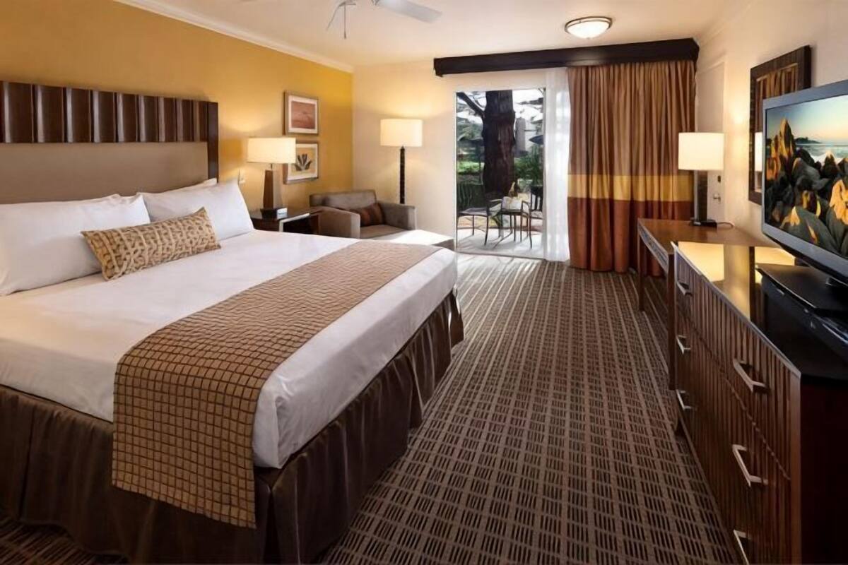 Quarto de hotel com uma cama grande, televisão, escrivaninha e vista para o exterior.