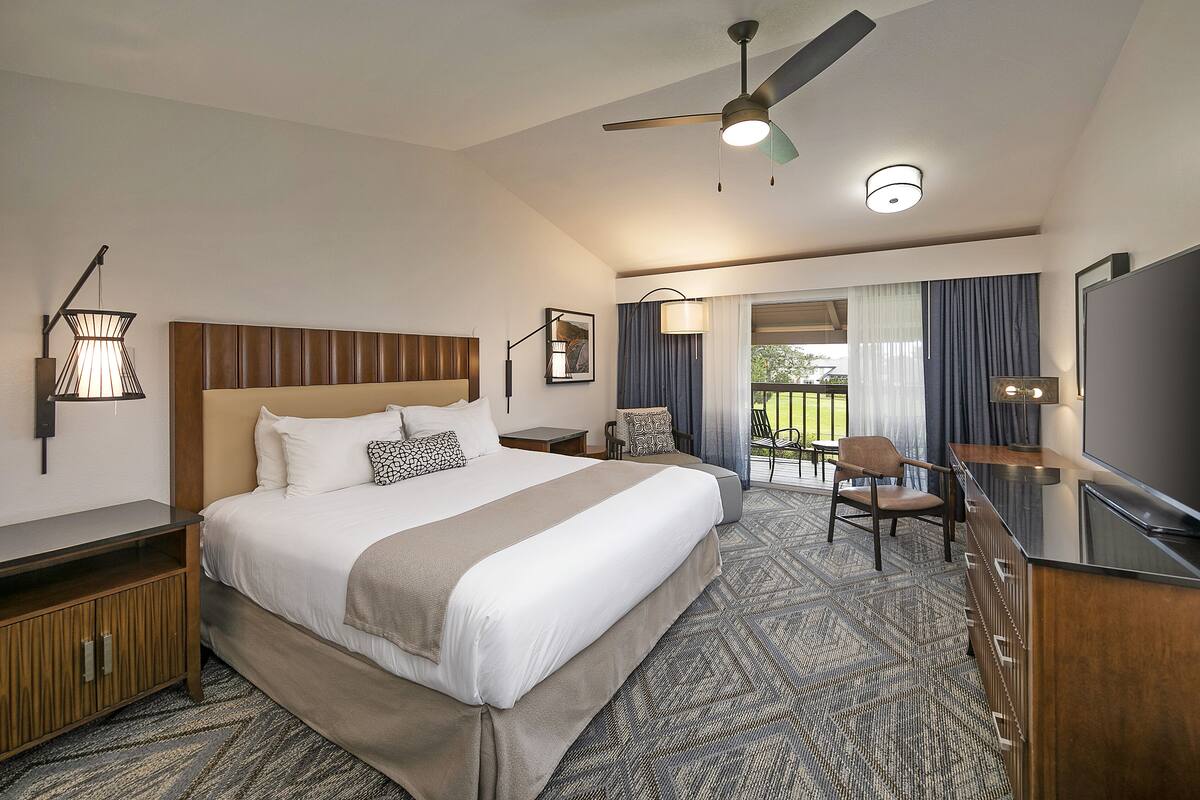 Quarto de hotel com uma cama grande, uma escrivaninha com televisão de tela plana, ventoinha no teto e vista para o exterior.