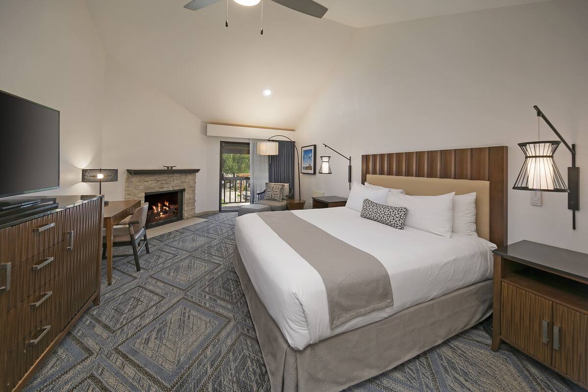 Quarto de hotel moderno com uma cama grande, lareira, televisão e varanda com área de estar ao ar livre.
