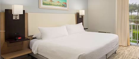 Habitación de hotel con una cama grande, dos mesitas de noche con lámparas, un cuadro en la pared y vista a zonas verdes por la ventana.