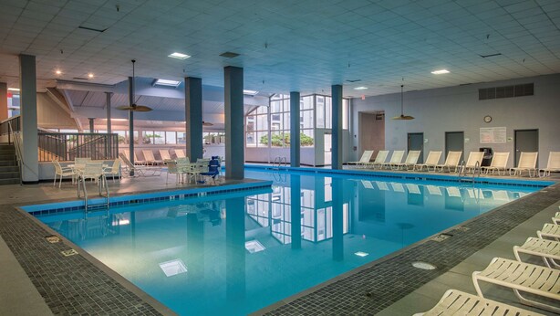 An indoor swimming pool with clear water, surrounded by lounge chairs and a staircase leading to upper levels. - Best Western Plus Strongsville Cleveland (Strongsville)