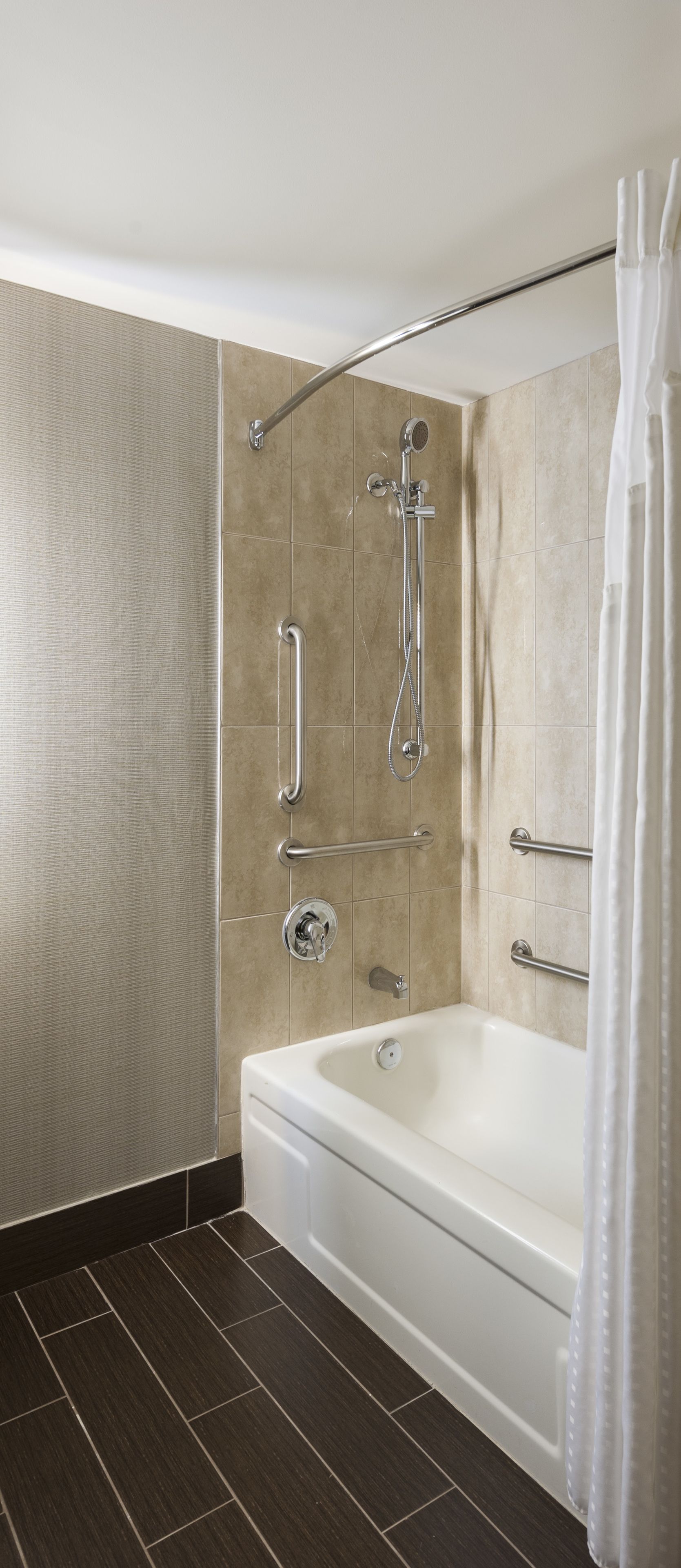 Une salle de bain moderne dotée d’une douche à l’italienne, de barres d’appui et d’une baignoire.