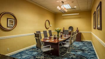 A conference room with a long table, chairs, a chandelier, and framed pictures on the walls.
