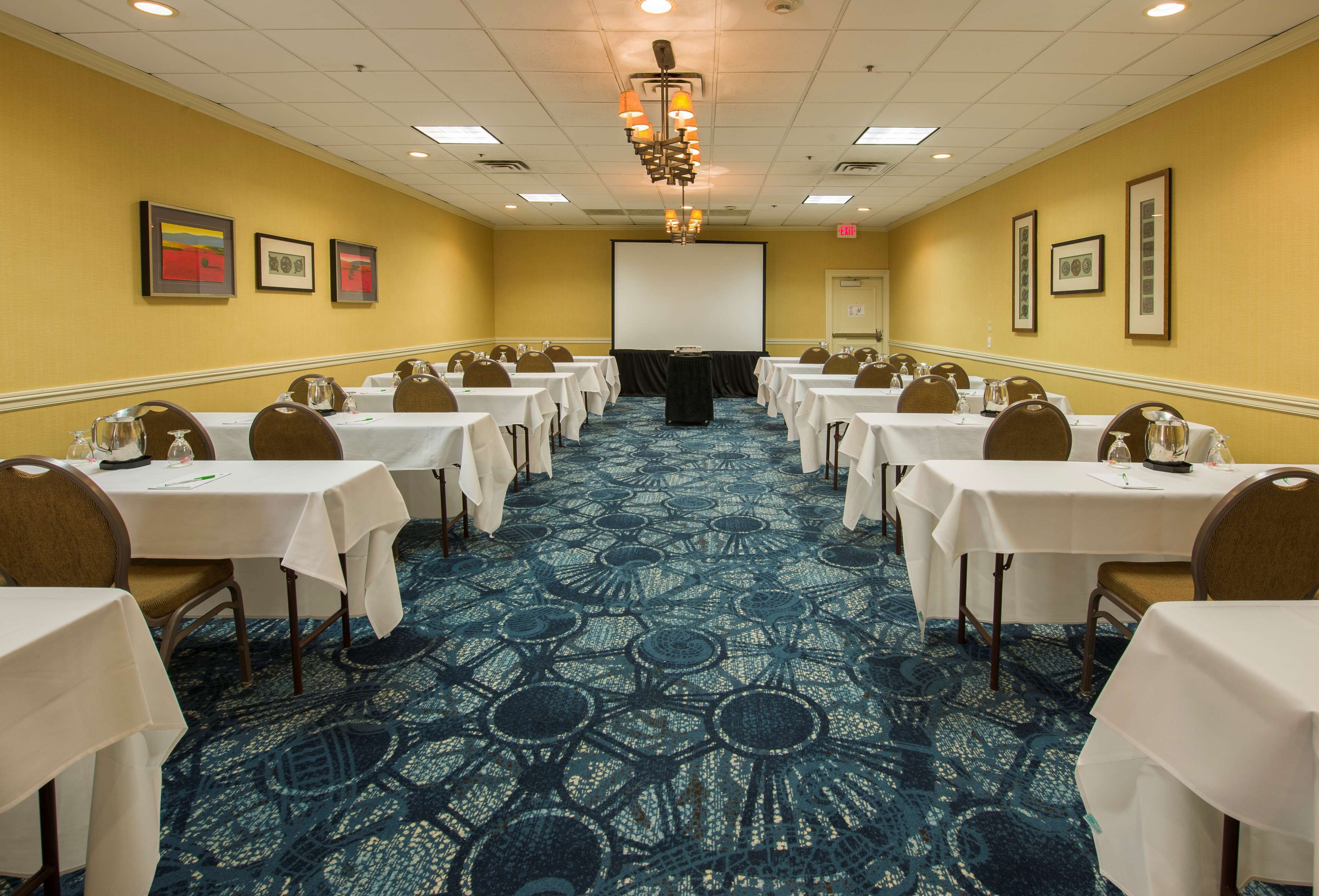 A conference room with tables set for a meeting, a projector screen, and framed artwork on the walls.
