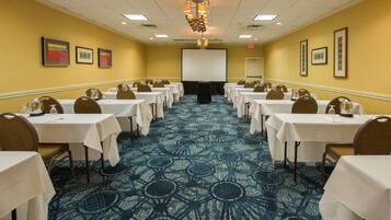 A conference room with tables set for a meeting, a projector screen, and framed artwork on the walls.