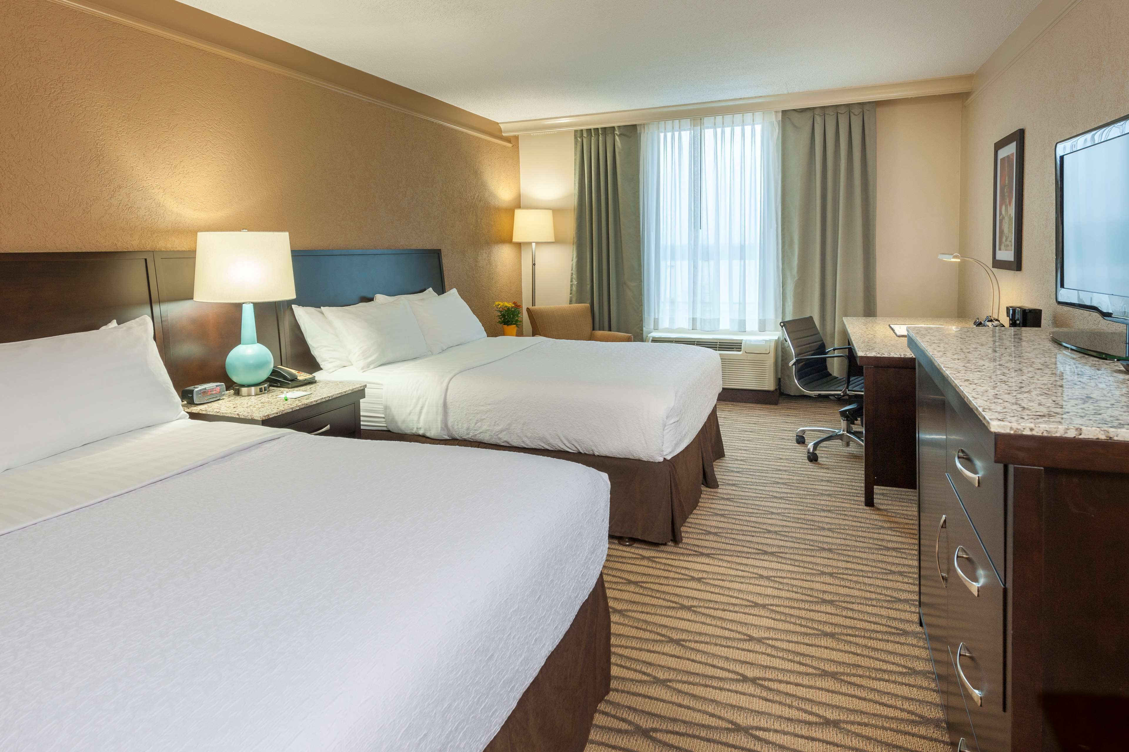A hotel room with two beds, a desk, a chair, a TV, and a window with curtains.