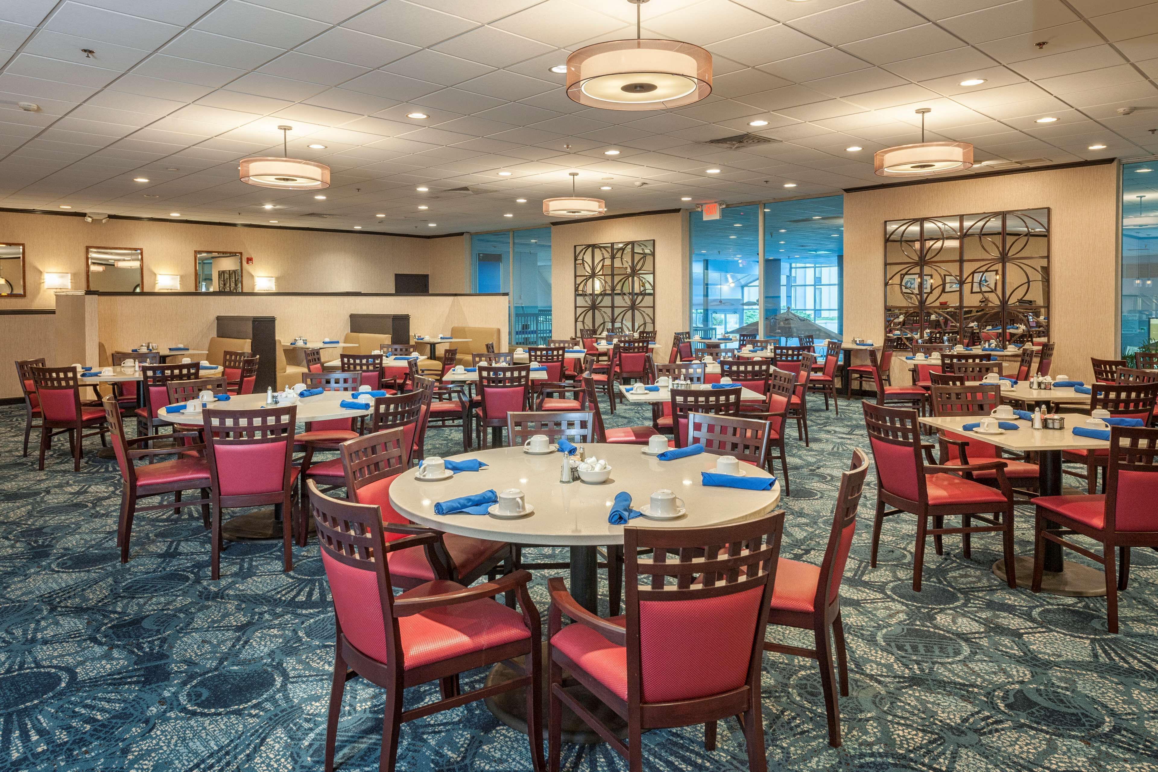 A hotel dining area with round tables, red chairs, and blue napkins.
