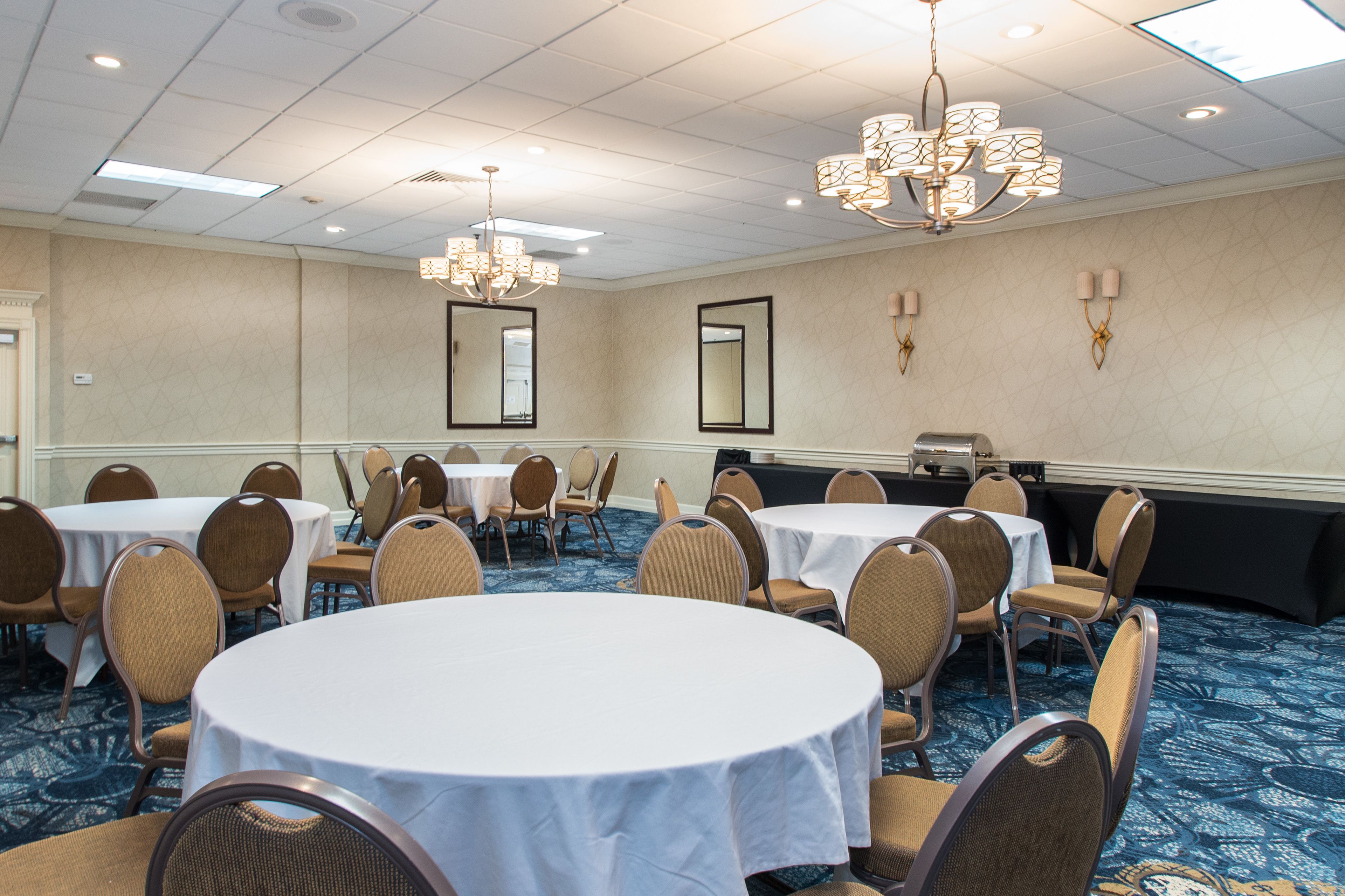 A conference room with round tables and chairs, a chandelier, and a large mirror on the wall.