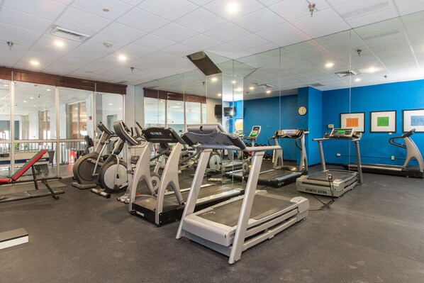 Un gimnasio con cintas de correr, elípticas y un banco rojo.