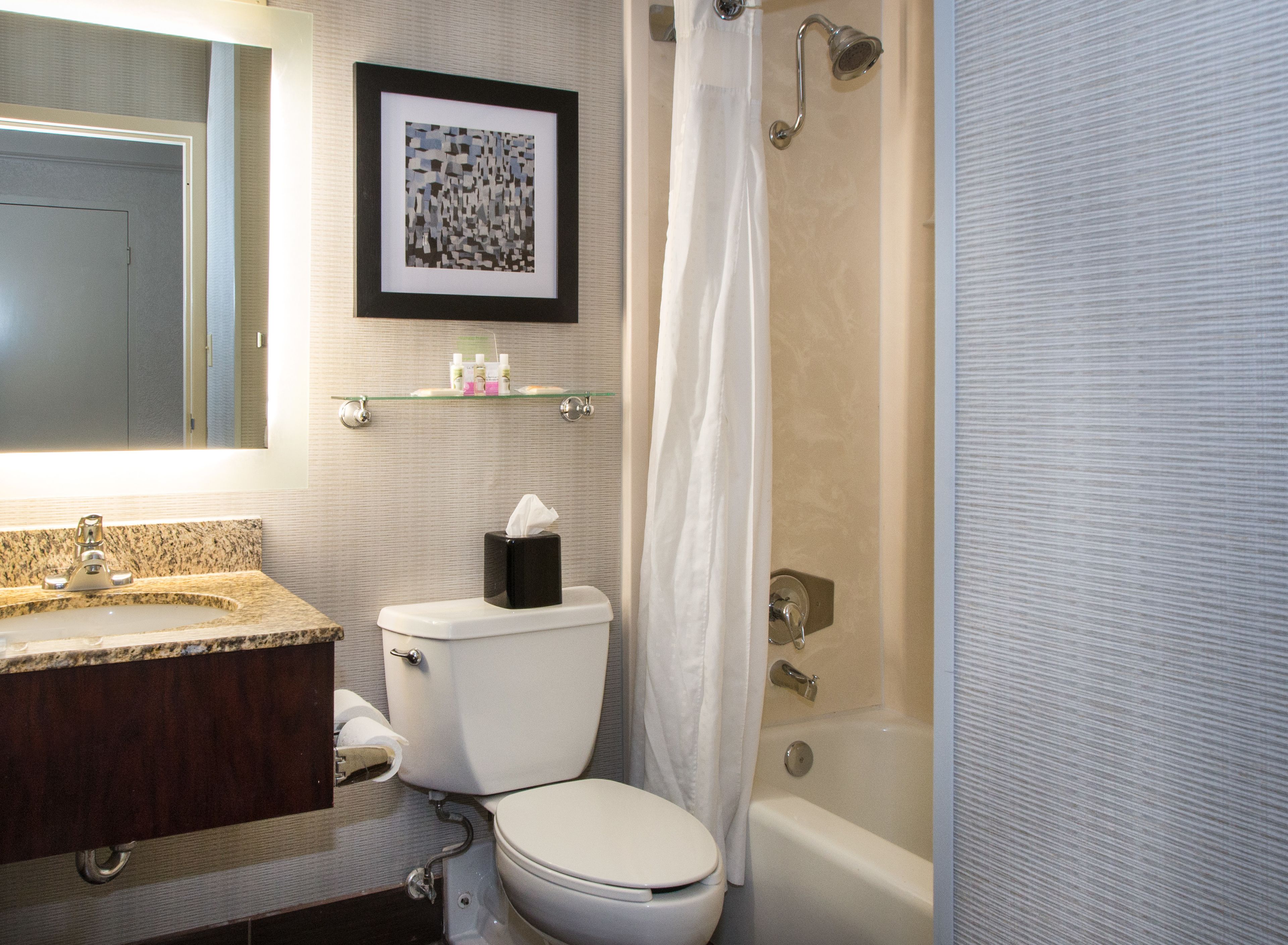 A bathroom with a toilet, sink, and bathtub. There is a framed picture on the wall above the toilet.