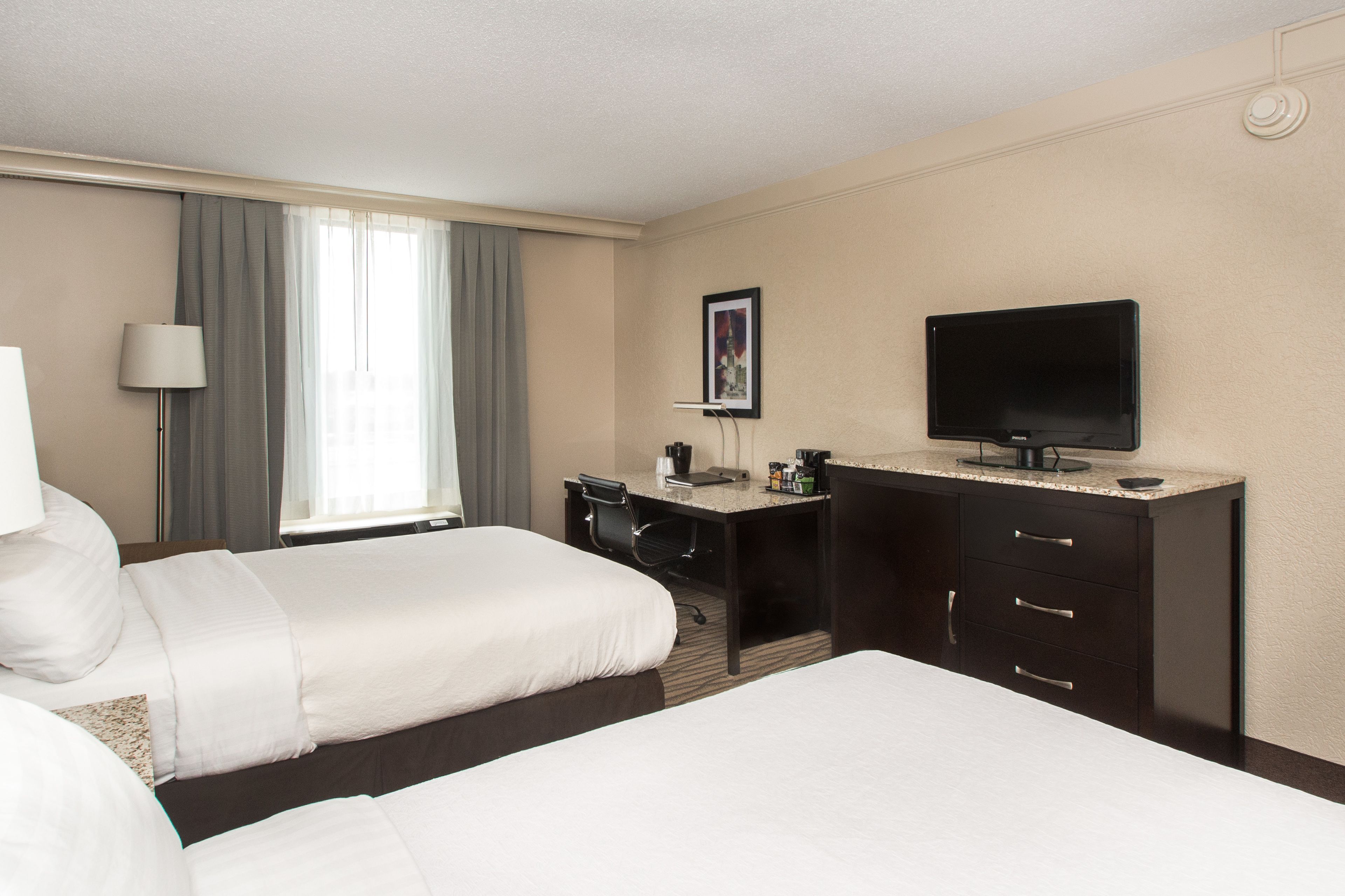 A hotel room with two beds, a desk, a television, and a window with curtains.