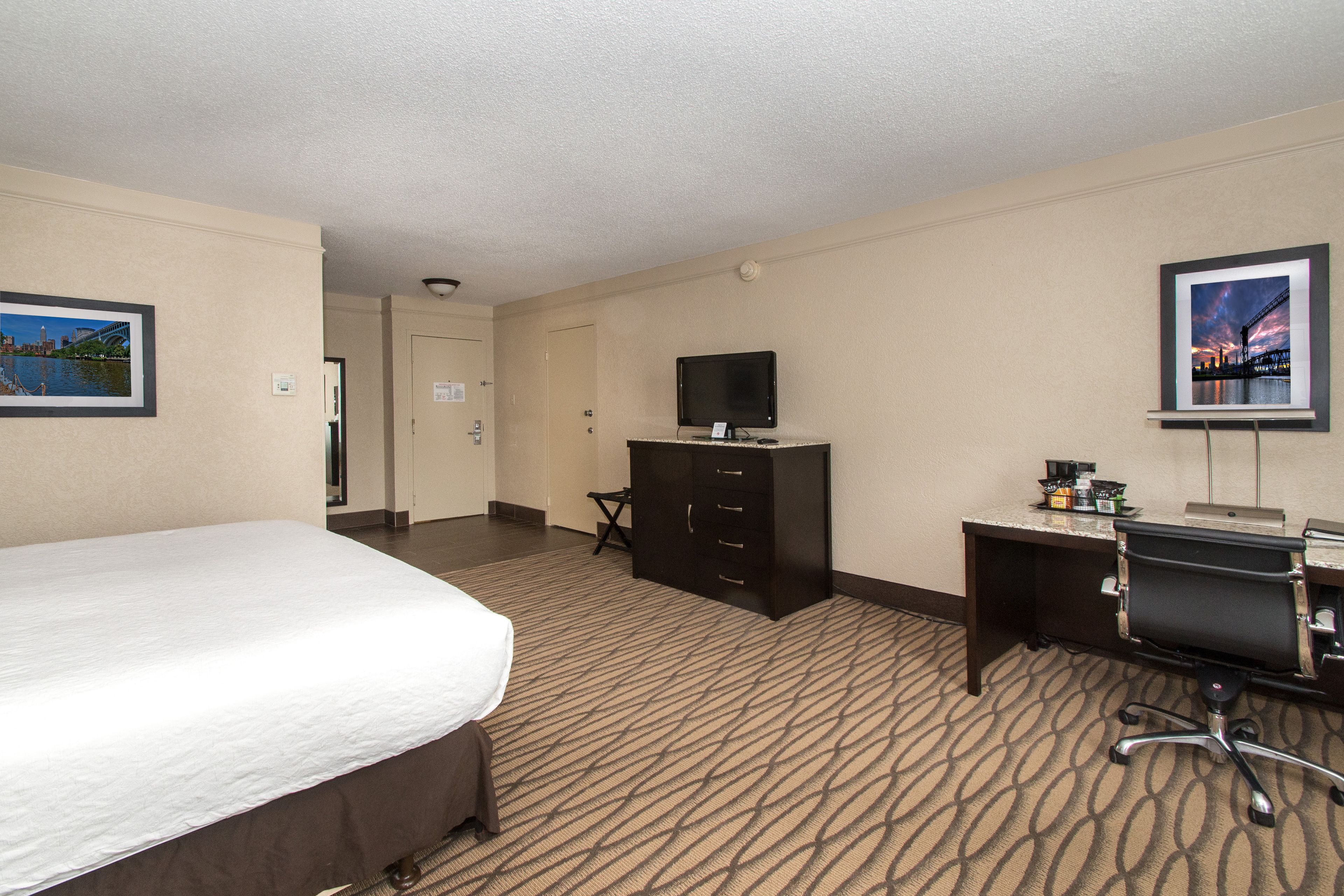 A hotel room with a bed, a desk with a computer, a television, and a dresser.