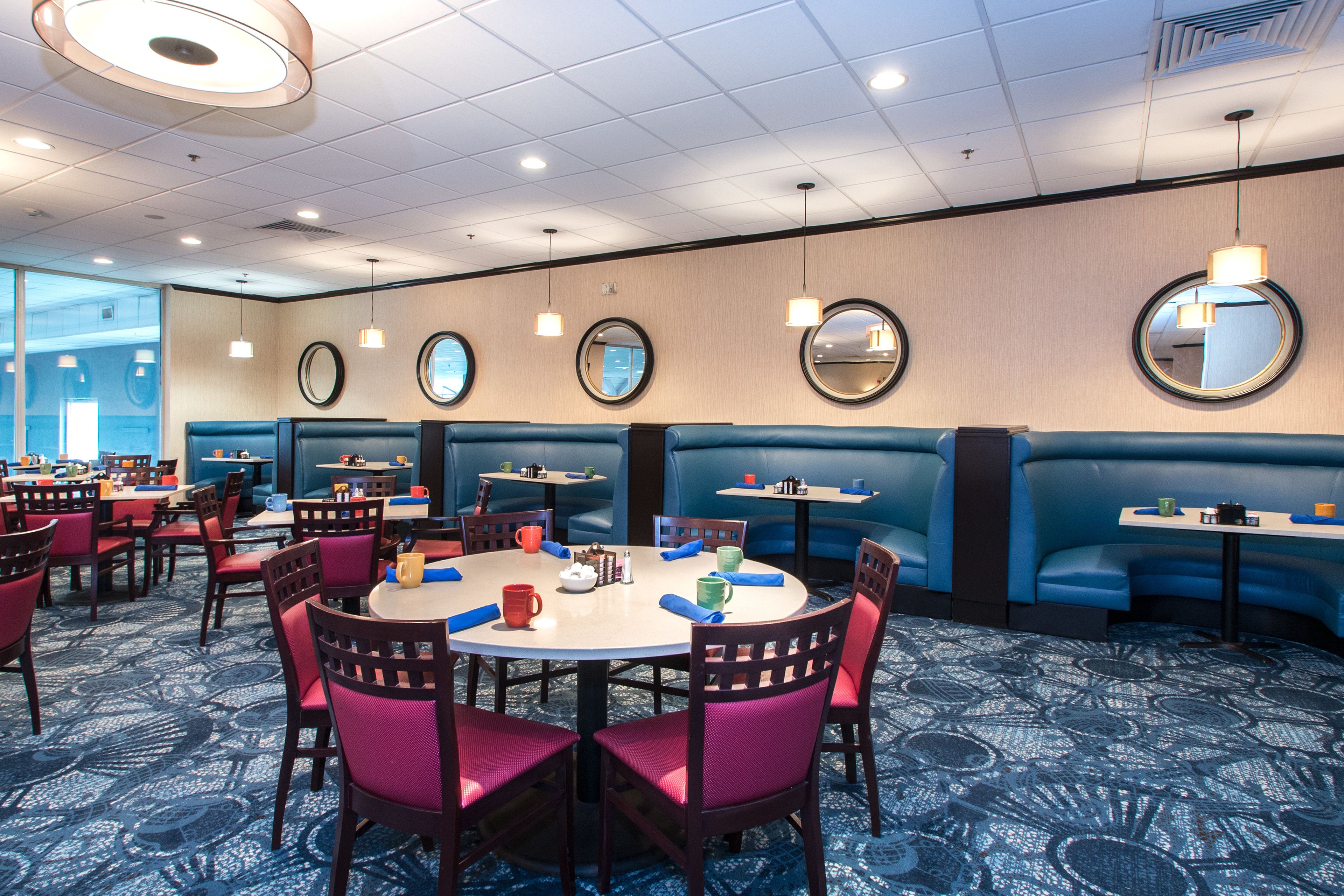 A hotel dining area with round tables, blue booths, and mirrored walls.