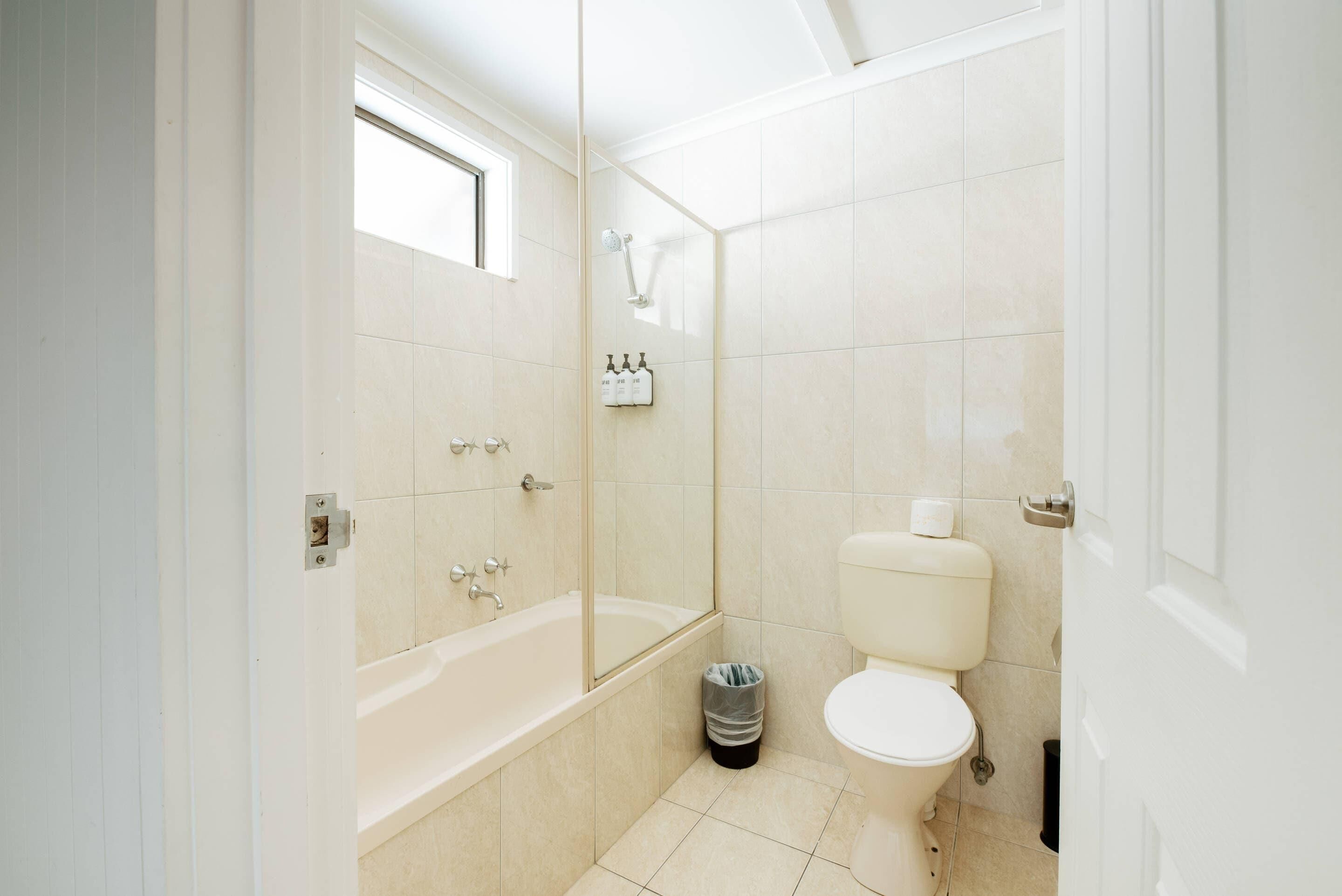 A bathroom with a bathtub, toilet, and a trash bin.