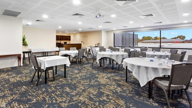 A conference room with multiple tables and chairs, a projector, and a large window with a view of the outside. - Quality Hotel Lakeside (Bendigo)