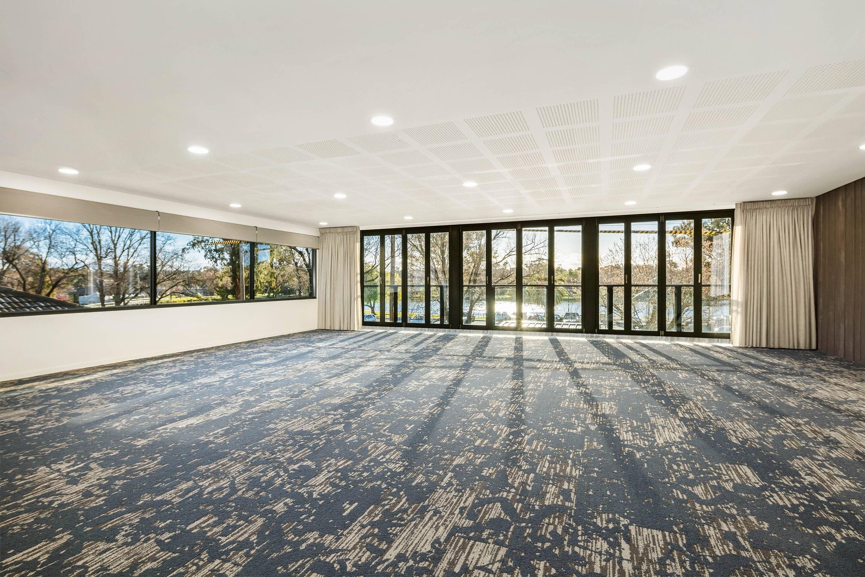 A spacious room with large windows, a patterned carpet, and a ceiling with recessed lighting.