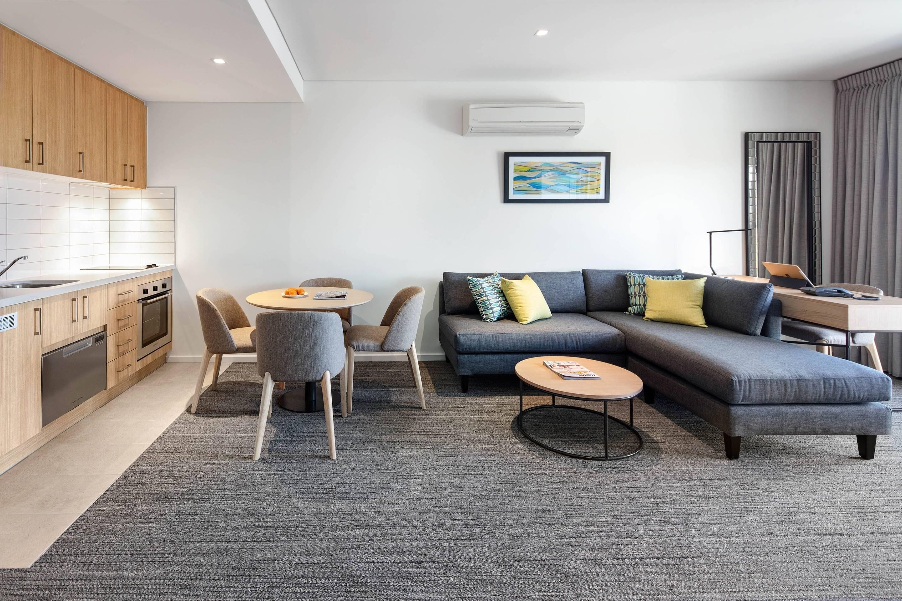 Una sala de estar moderna con un sofá gris, una mesa redonda para café y un comedor con sillas y una mesa.