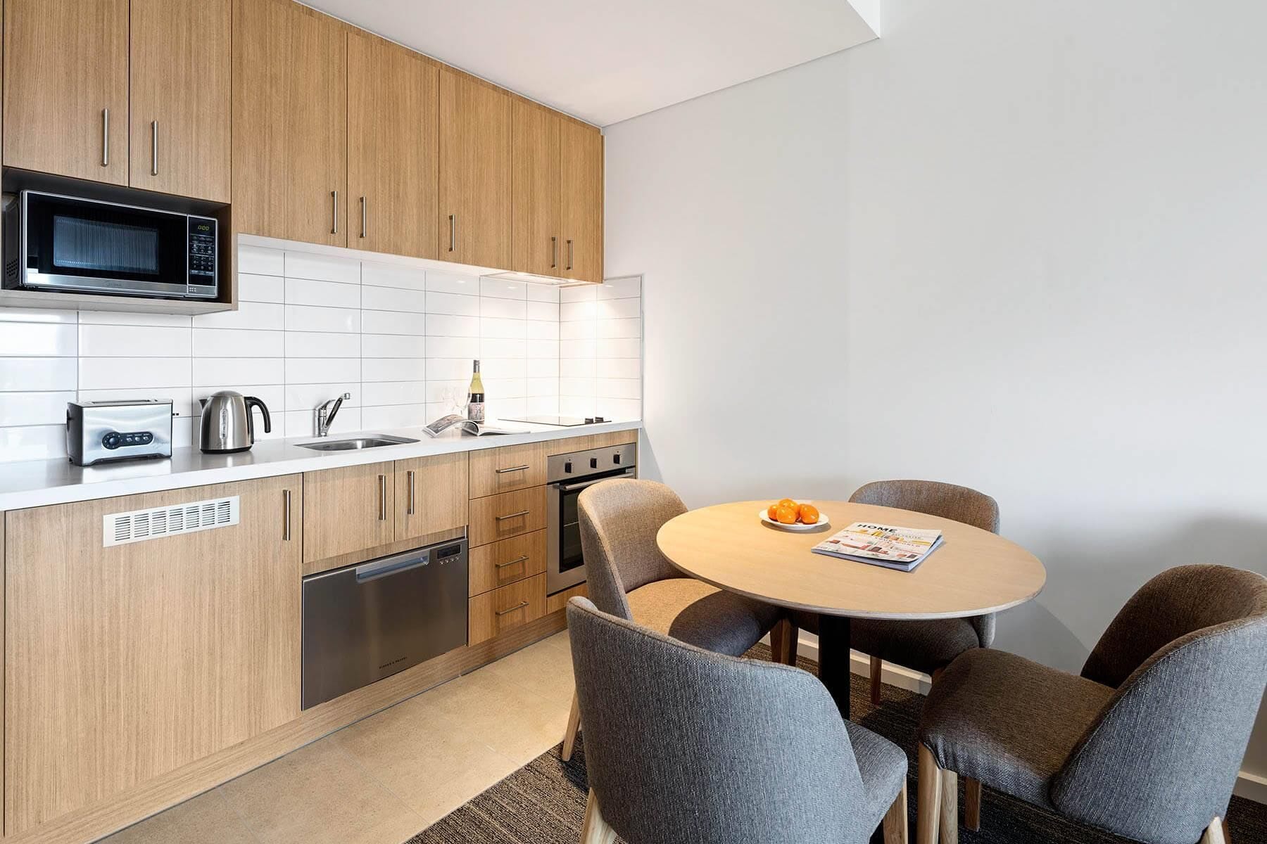 Une cuisine moderne équipée d’un four à micro-ondes, d’un grille-pain, d’une bouilloire et d’un évier. On y trouve une table à manger avec quatre chaises, ainsi qu’un magazine.