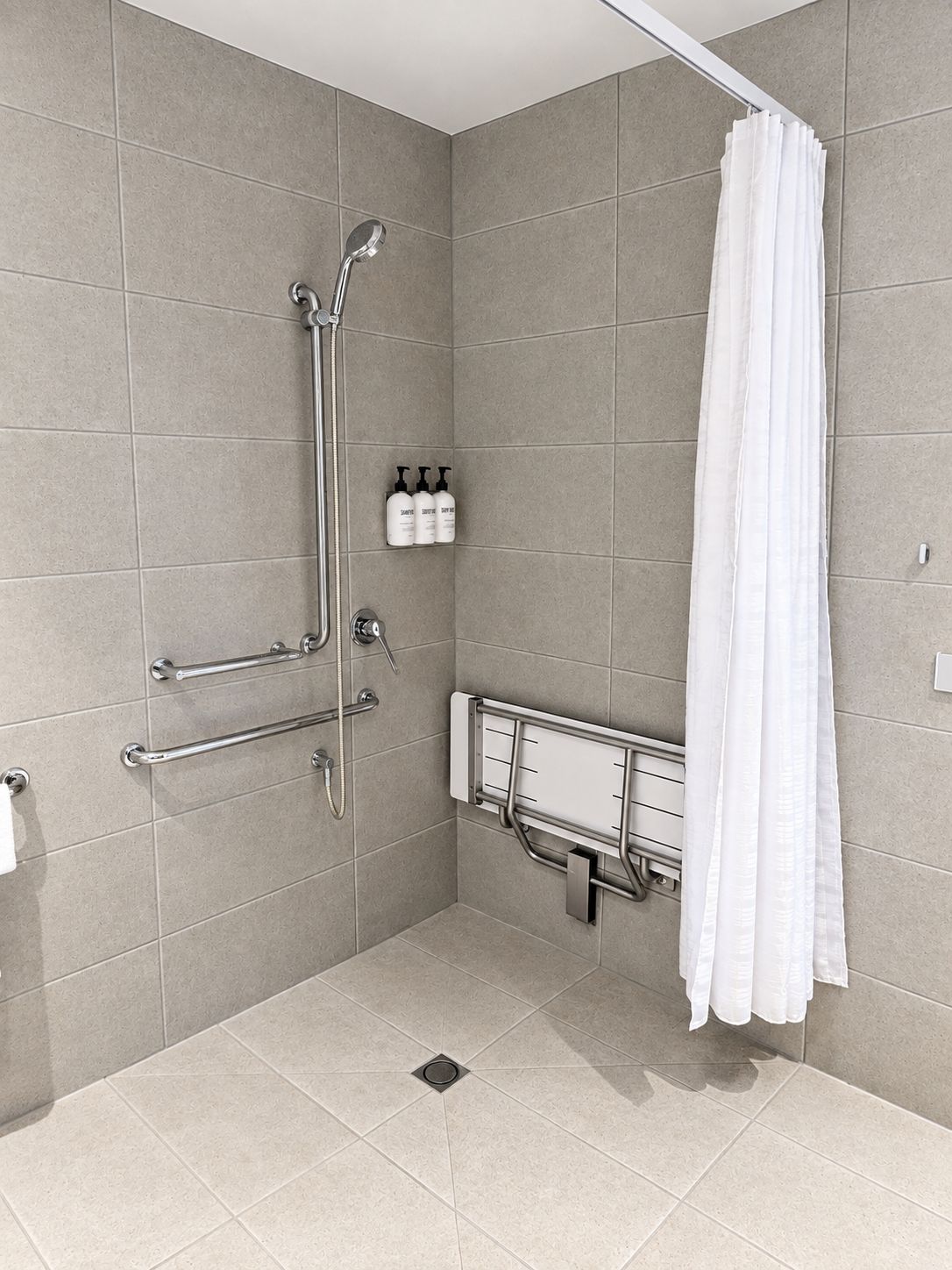 A shower area with a white shower curtain, grab bars, and a handheld showerhead.