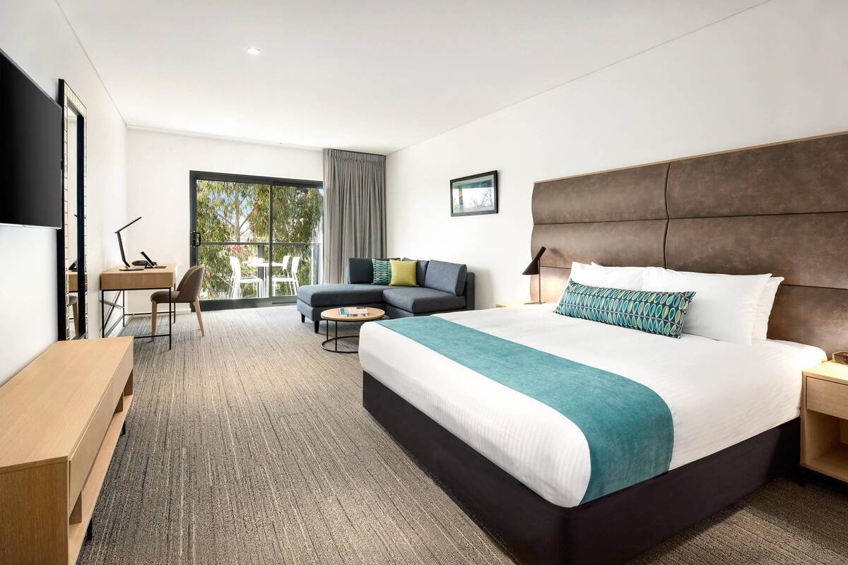 Ein modernes Hotelzimmer mit einem großen Bett, einem Schreibtisch, einer Sitzecke und Blick ins Freie.