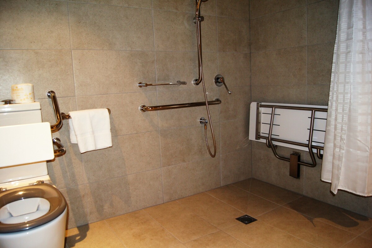 Un baño con inodoro, ducha con barras de apoyo y perchero para toallas.