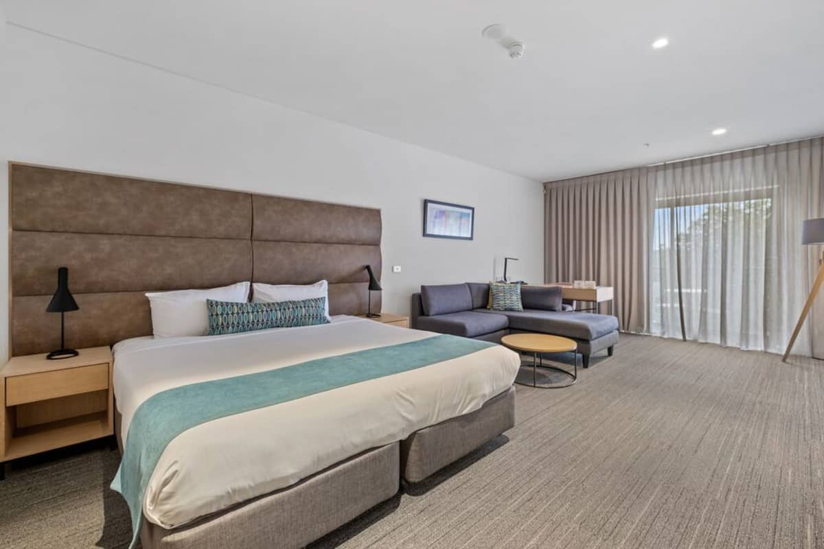 Ein modernes Hotelzimmer mit einem großen Bett, einer Couch, einem kleinen runden Tisch und einem Schreibtisch.