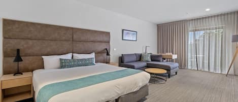 Quarto de hotel moderno com uma cama grande, um sofá, uma pequena mesa redonda e uma escrivaninha.