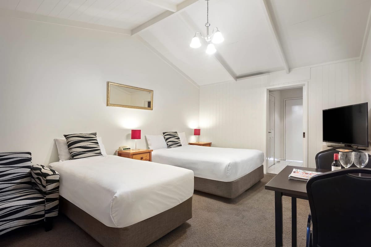 Ein Hotelzimmer mit zwei Betten, einem Fernseher, einem Schreibtisch mit Stuhl und einem Spiegel an der Wand.