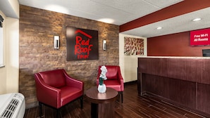 A Red Roof Inn reception area with a stone wall, two red chairs, a reception desk, and a sign indicating free Wi-Fi in all rooms.