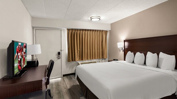 A hotel room with a bed, a desk with a television, a lamp, and a window with curtains.