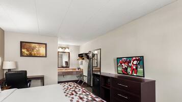 A hotel room with a bed, a desk, a chair, a TV, a mirror, and a painting on the wall.