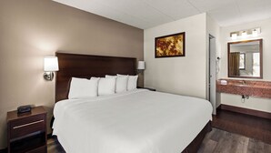 A hotel room with a large bed, bedside lamps, a painting on the wall, a bathroom with a mirror and sink, and a door leading to another room. - Red Roof Inn Springfield, IL (Springfield)