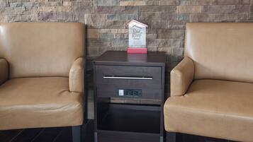 A hotel room with two leather armchairs, a small wooden nightstand with a Red Roof Inn sign, and a built-in drawer unit.