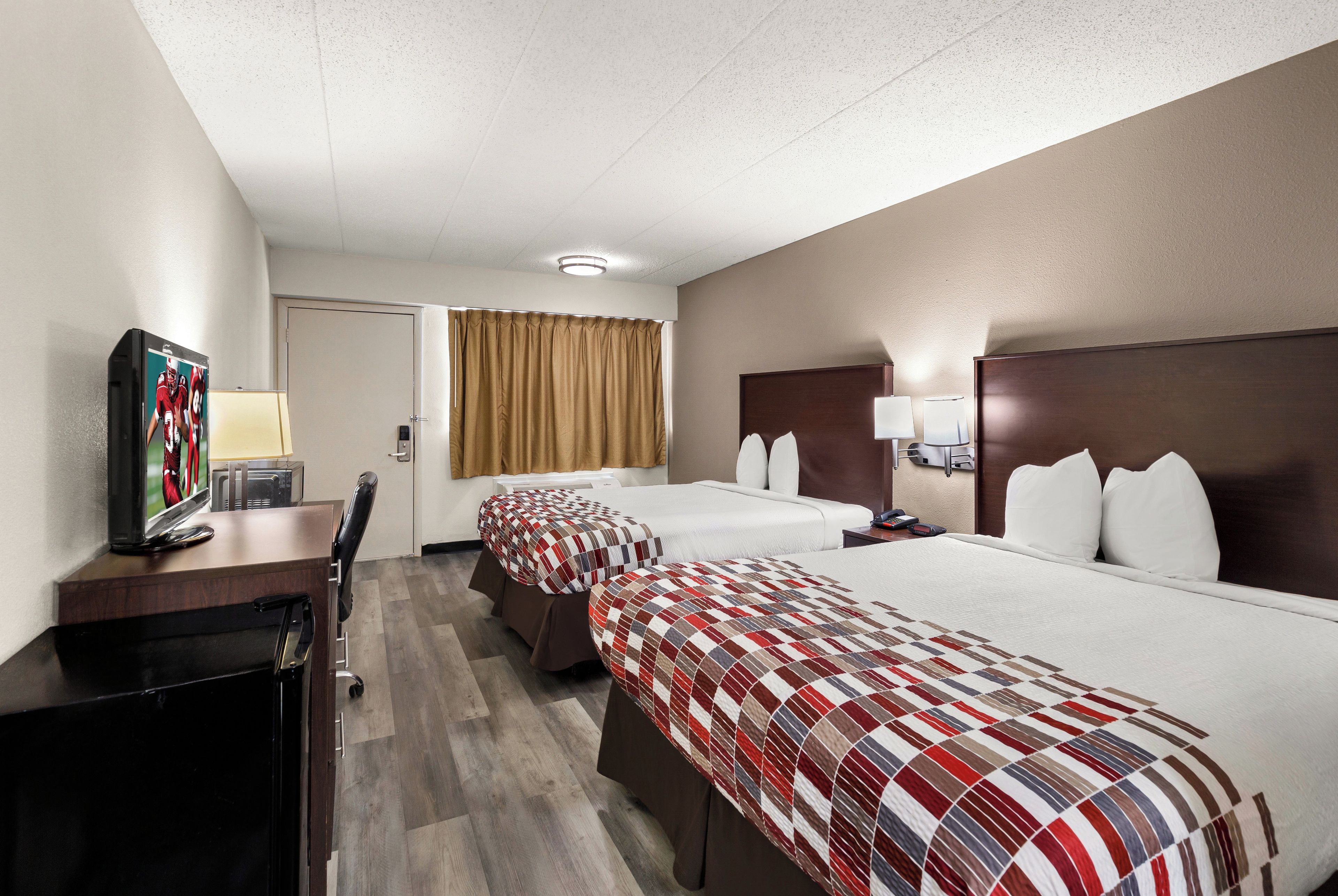 Habitación de hotel con dos camas, un escritorio, televisor, lámpara y ventana con cortinas.