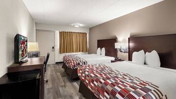 Habitación de hotel con dos camas, un escritorio, televisor, lámpara y ventana con cortinas.