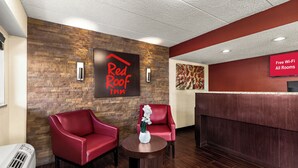 A Red Roof Inn reception area with a brick wall, two red armchairs, a small table with a vase, and a sign indicating free Wi-Fi. - Red Roof Inn Springfield, IL (Springfield)