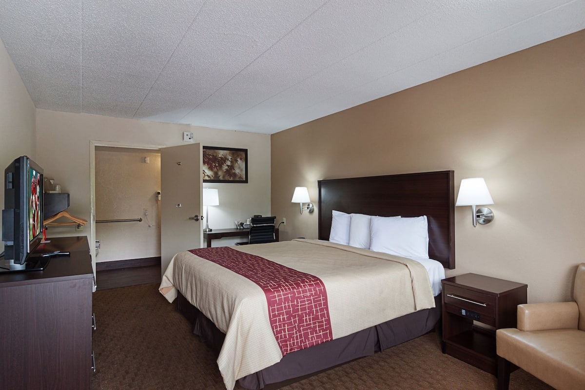 A hotel room with a bed, bedside lamps, a desk with a computer, a TV, and a chair.