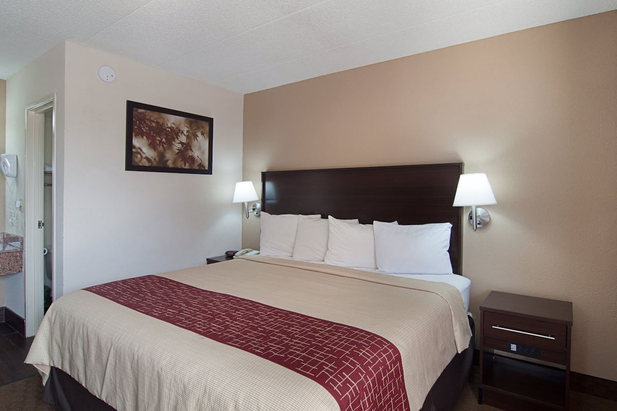 A hotel room with a bed, bedside tables, a nightstand, a wall-mounted lamp, a framed picture, and a small cabinet.
