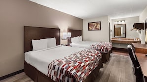 A hotel room with two beds, a desk, a chair, a mirror, and a bathroom with a sink and towel rack.