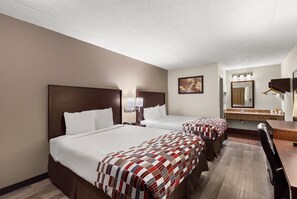 A hotel room with two beds, a desk, a chair, a mirror, and a bathroom with a sink and towel rack. - Red Roof Inn Springfield, IL (Springfield)