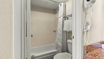 A bathroom with a bathtub, toilet, and a hairdryer mounted on the wall.