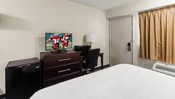A hotel room with a bed, a desk with a computer, a television, a lamp, and a heater.