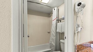 A bathroom with a bathtub, toilet, and a hairdryer on the wall.