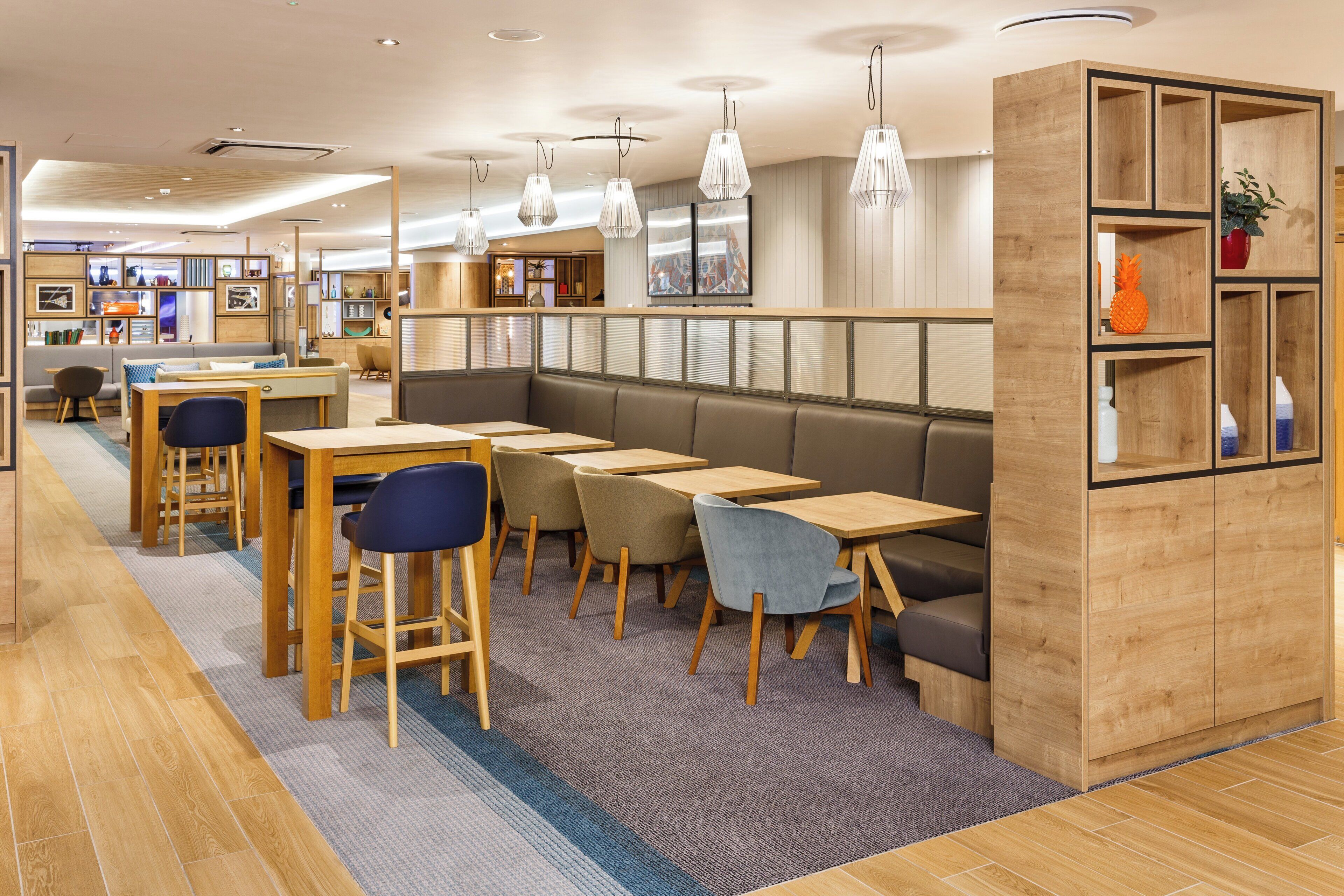 A modern interior with wooden tables and chairs, a seating area with a sofa, and pendant lighting.