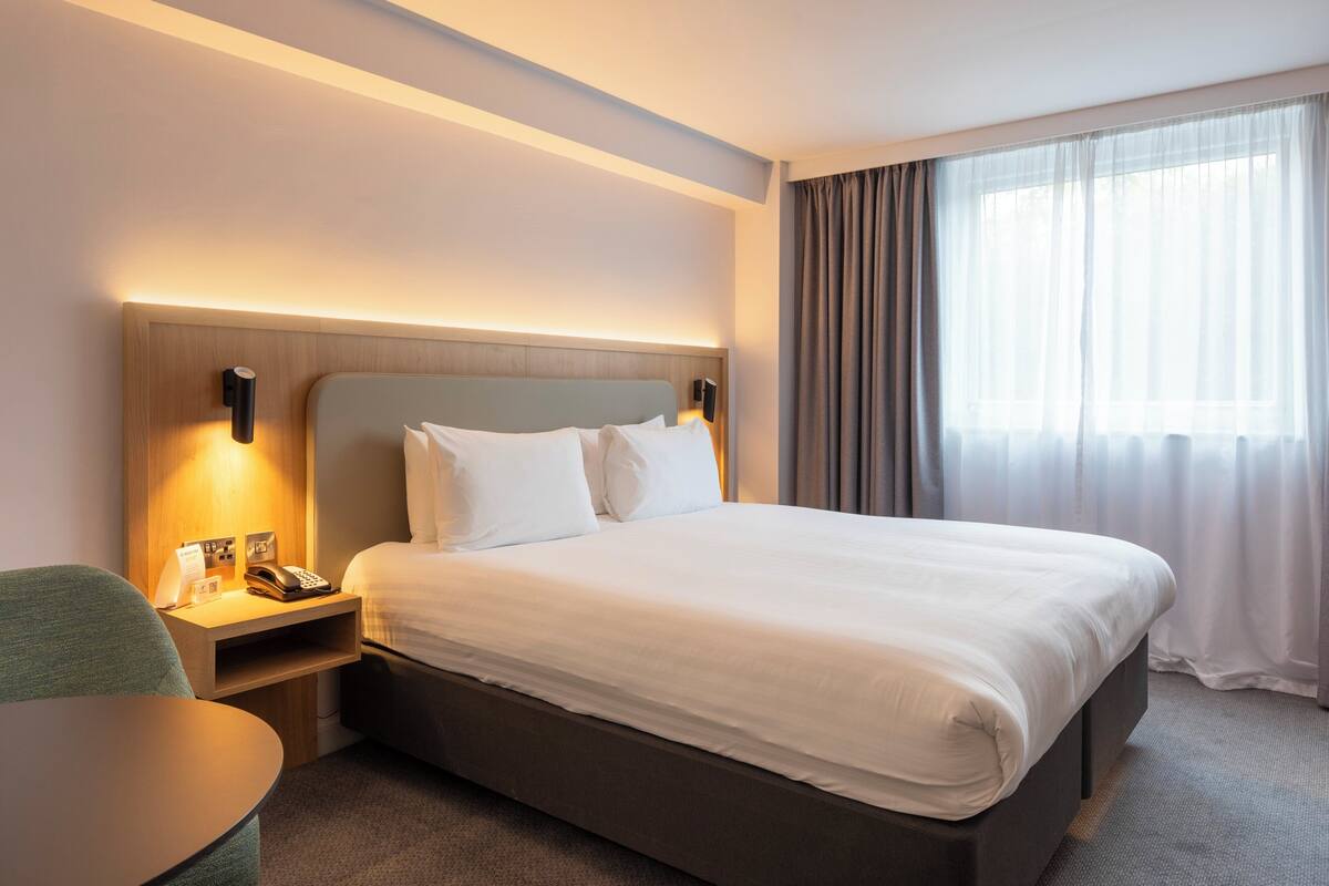 Une chambre d’hôtel avec un grand lit, des tables de chevet, un bureau et une fenêtre avec des rideaux.