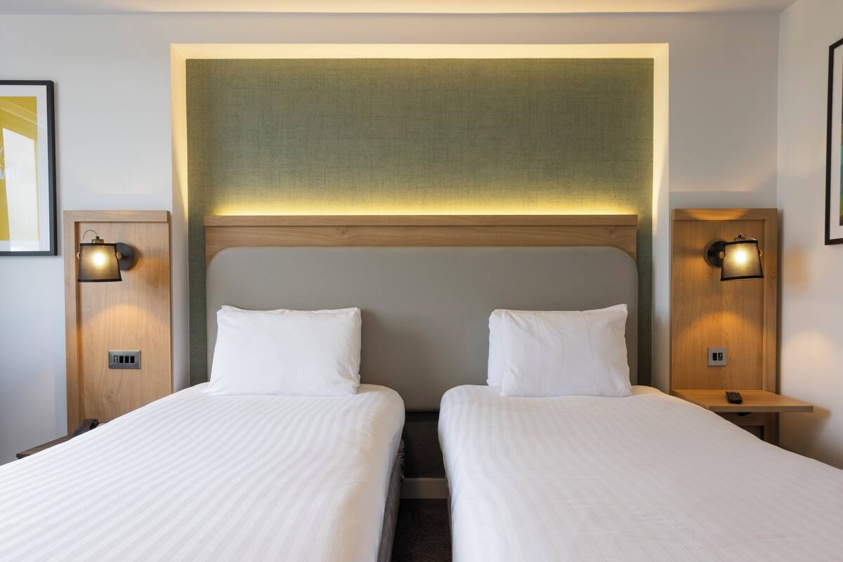 Une chambre d’hôtel avec deux lits, des tables de chevet et des lampes fixées au mur.