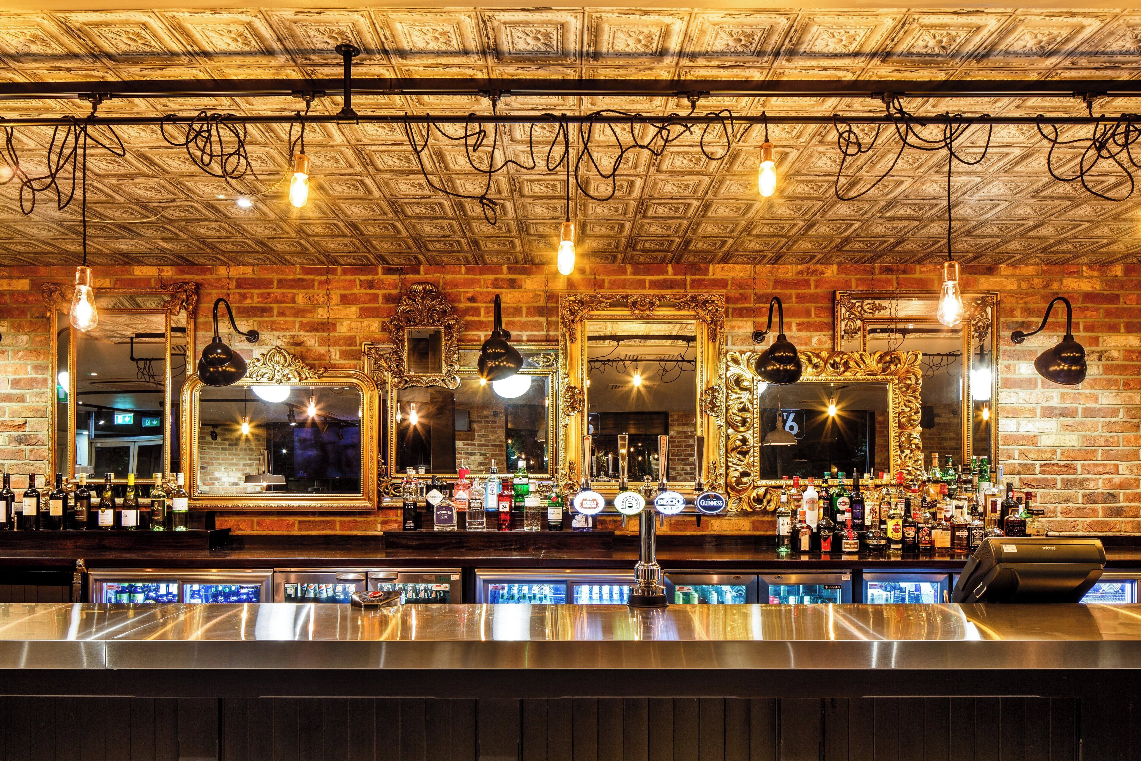 Un bar con múltiples espejos, una pared de ladrillo y una variedad de botellas y vasos.