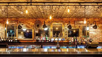 Un bar con múltiples espejos, una pared de ladrillo y una variedad de botellas y vasos.