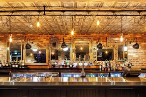 A bar with multiple mirrors, a brick wall, and a variety of bottles and glasses. - Holiday Inn London - Heathrow M4,jct.4 by IHG (West Drayton)